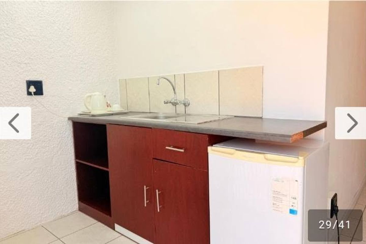 A compact kitchenette area featuring a stainless steel sink, tiled backsplash, and basic built-in cabinetry with a laminate countertop.