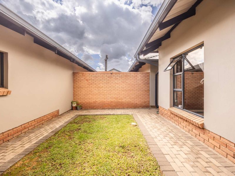 A private rear courtyard featuring a paved walkway, central lawn area, and enclosed by brick boundary walls.