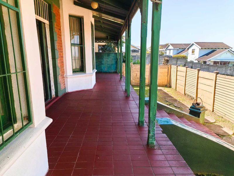 A covered veranda featuring tiled flooring and timber support posts, overlooking a side garden area with a precast concrete boundary wall.