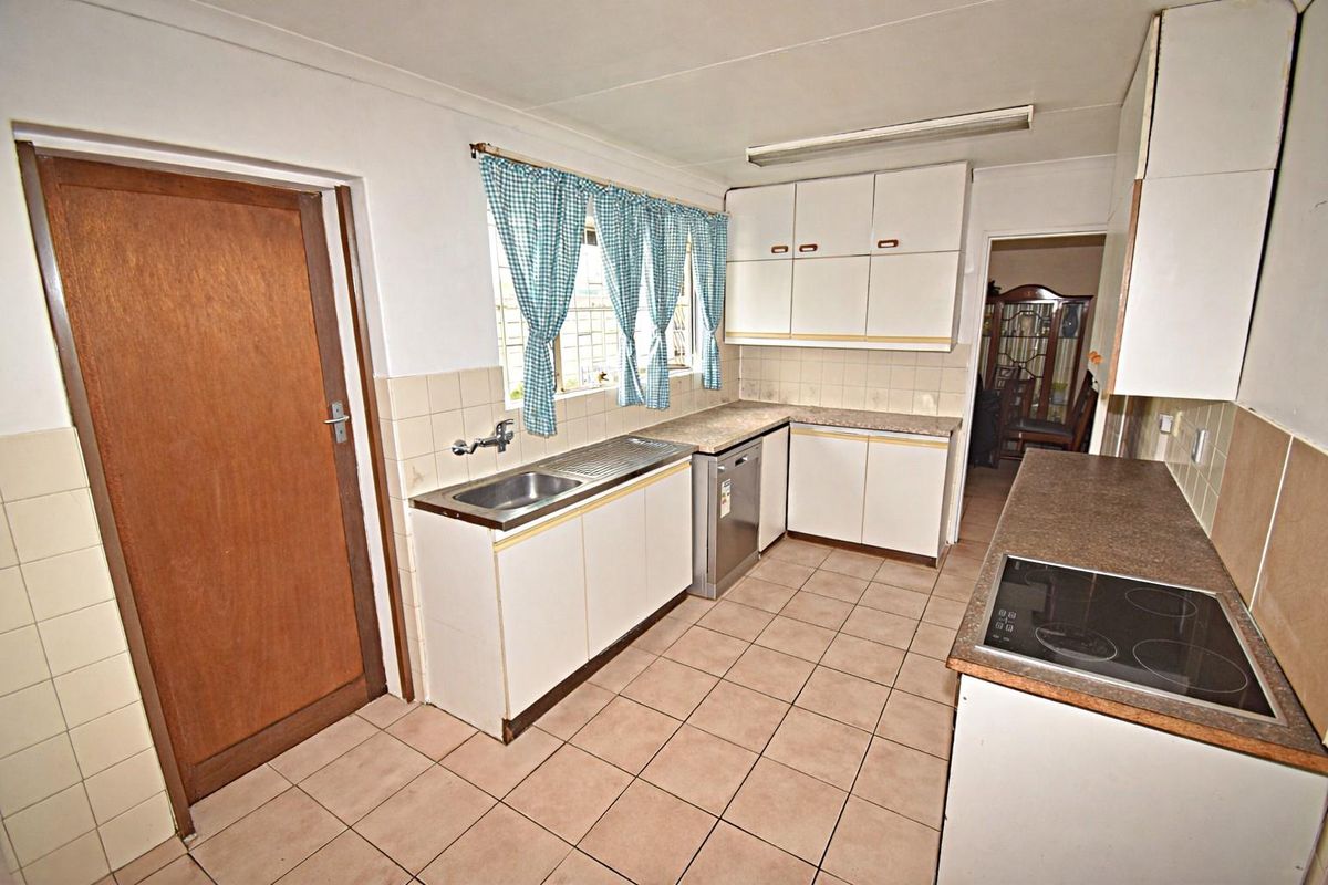 A functional kitchen featuring white cabinetry, laminate countertops, a built-in electric hob, and tiled flooring with direct access to adjacent living areas.