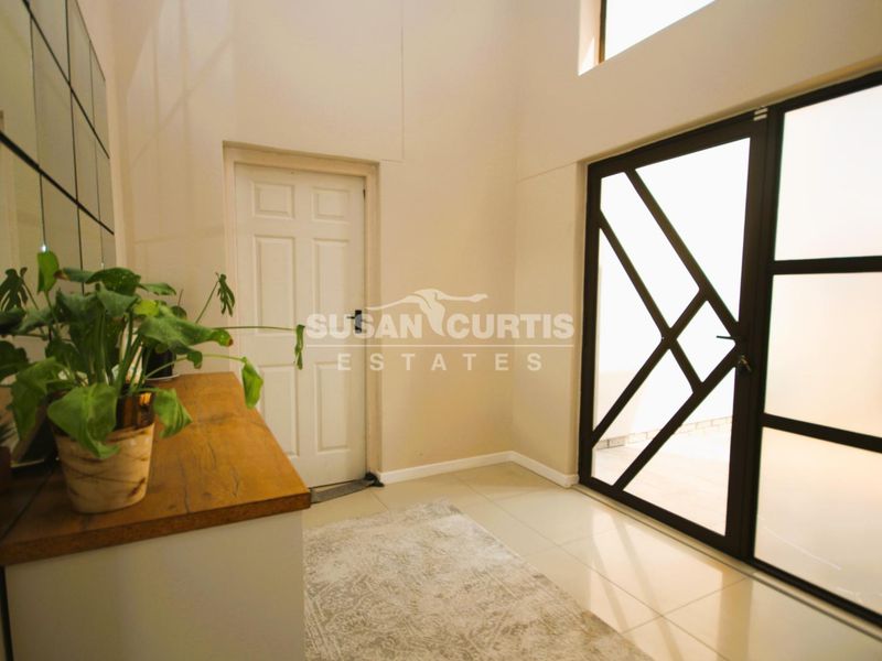 A bright and spacious entrance hall featuring high ceilings, tiled flooring, and a modern geometric glass front door.