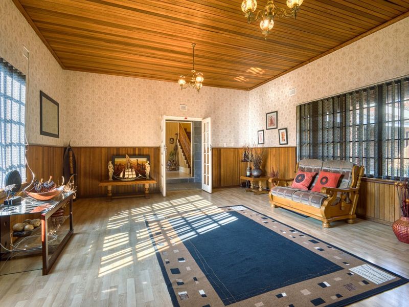 Spacious living room featuring timber tongue and groove ceilings, wood wall paneling, and laminate flooring, offering a traditional aesthetic with ample natural light.