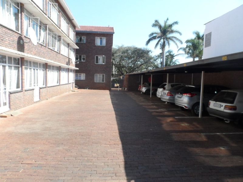 Exterior view of the apartment complex featuring a brick-paved courtyard and covered parking bays for residents.