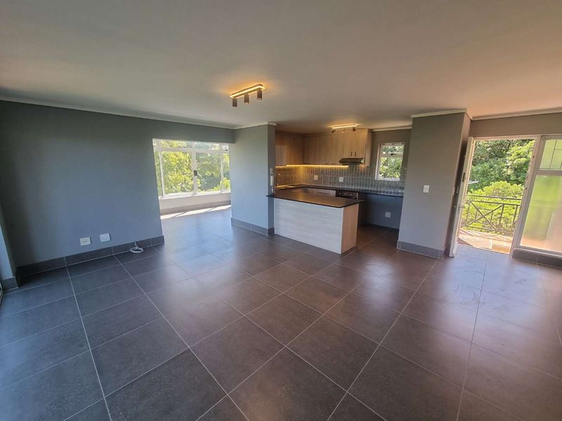 Spacious open-plan living area featuring modern tiled floors, a contemporary kitchen with built-in cabinetry, and direct access to a private balcony.