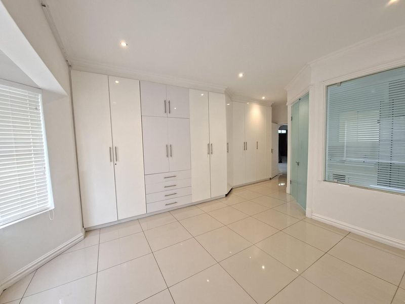 Spacious bedroom featuring extensive built-in cabinetry, neutral tiled flooring, and modern recessed lighting, offering a clean and versatile living space.