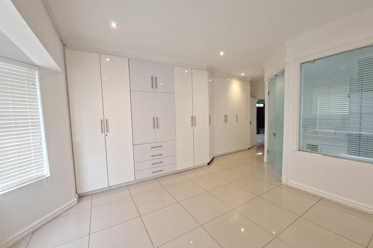 Spacious bedroom featuring extensive built-in cabinetry, neutral tiled flooring, and modern recessed lighting, offering a clean and versatile living space.