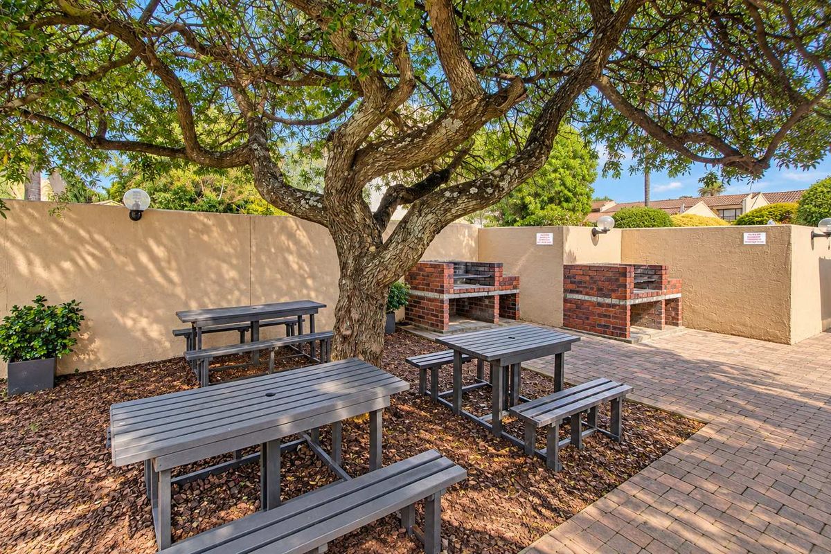 Communal outdoor entertainment area featuring brick built-in braais, paved flooring, and mature trees within a secure boundary wall setting.