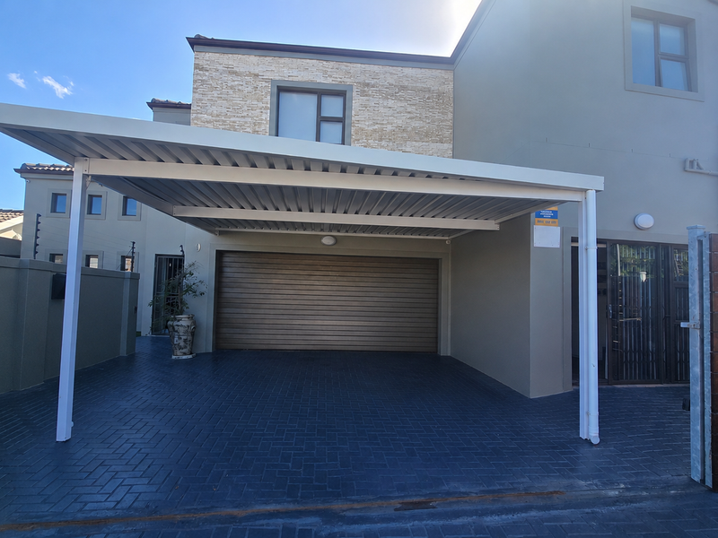 Modern front elevation featuring a covered carport, paved driveway, stone-clad facade, and secure timber fencing.