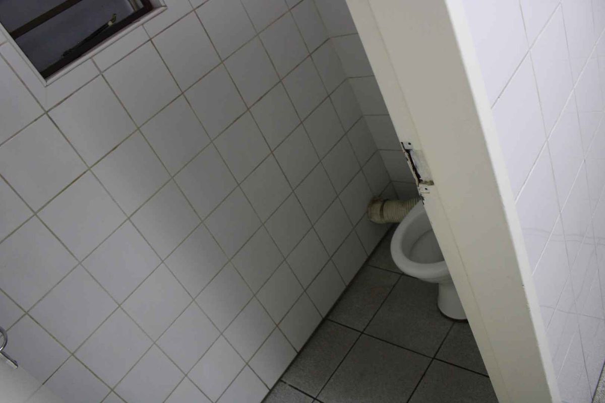 A small, tiled bathroom featuring a toilet and exposed plumbing, requiring maintenance and cosmetic updates.