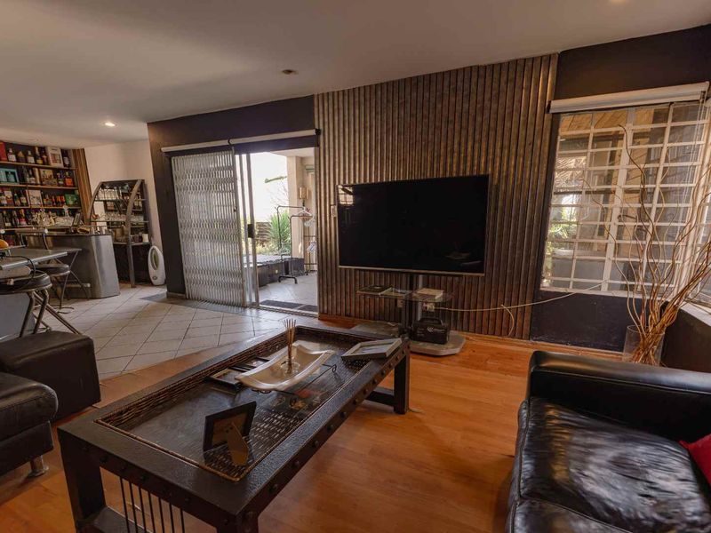 Living room featuring laminate flooring, a vertical slat feature wall, and an integrated bar area with access to an outdoor patio.