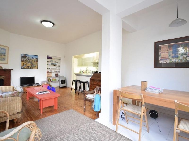 Open-plan living and dining area featuring hardwood and tiled flooring, a fireplace mantel, and built-in shelving, with an adjacent kitchen space.