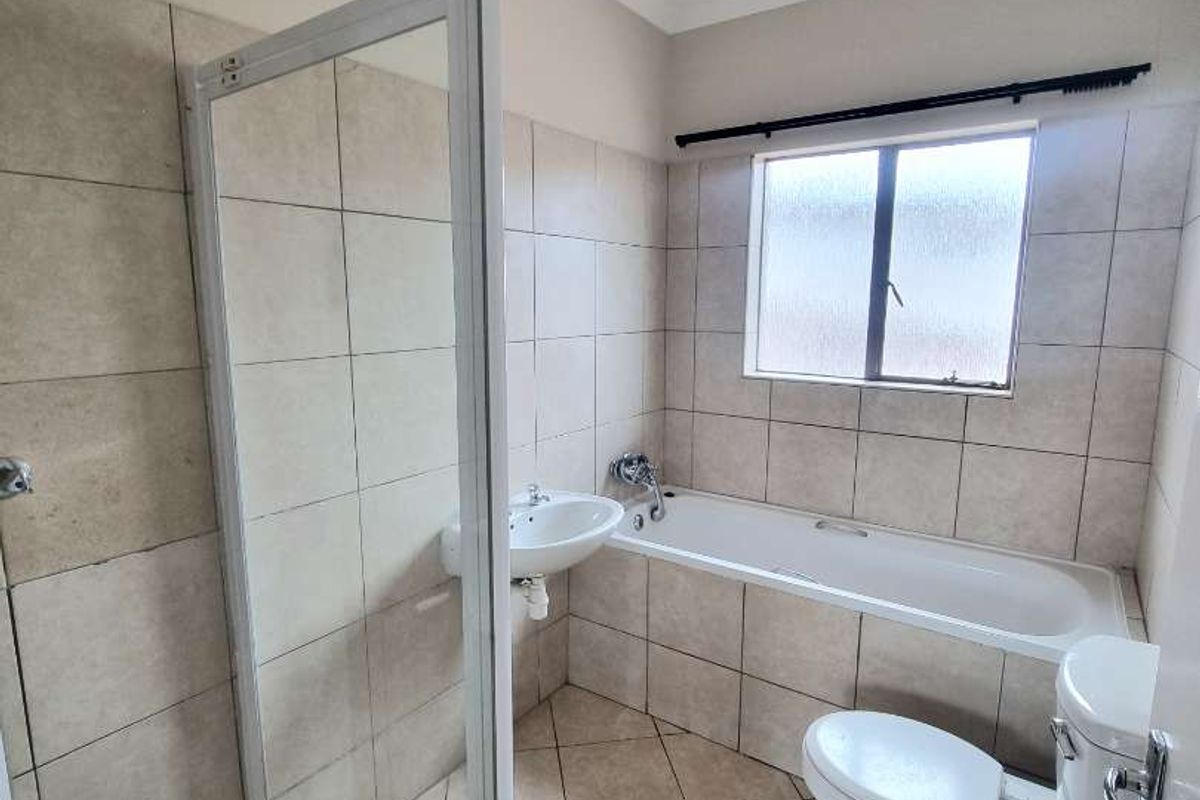 A functional bathroom featuring a glass-enclosed shower, a built-in bathtub, a pedestal basin, and a toilet with neutral wall and floor tiling.