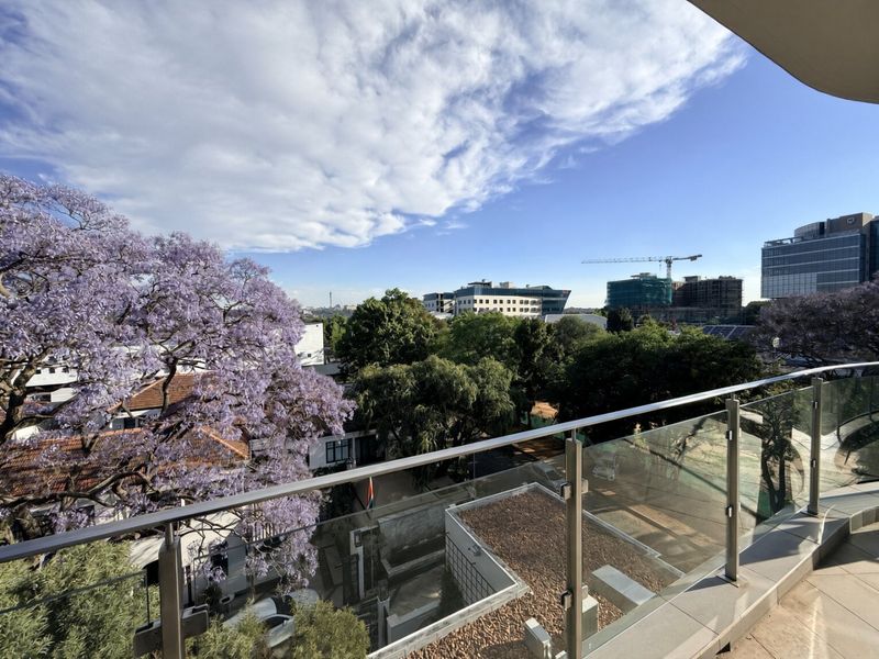 A spacious balcony featuring a modern glass balustrade and tiled flooring, offering an elevated view of the surrounding neighborhood and cityscape.