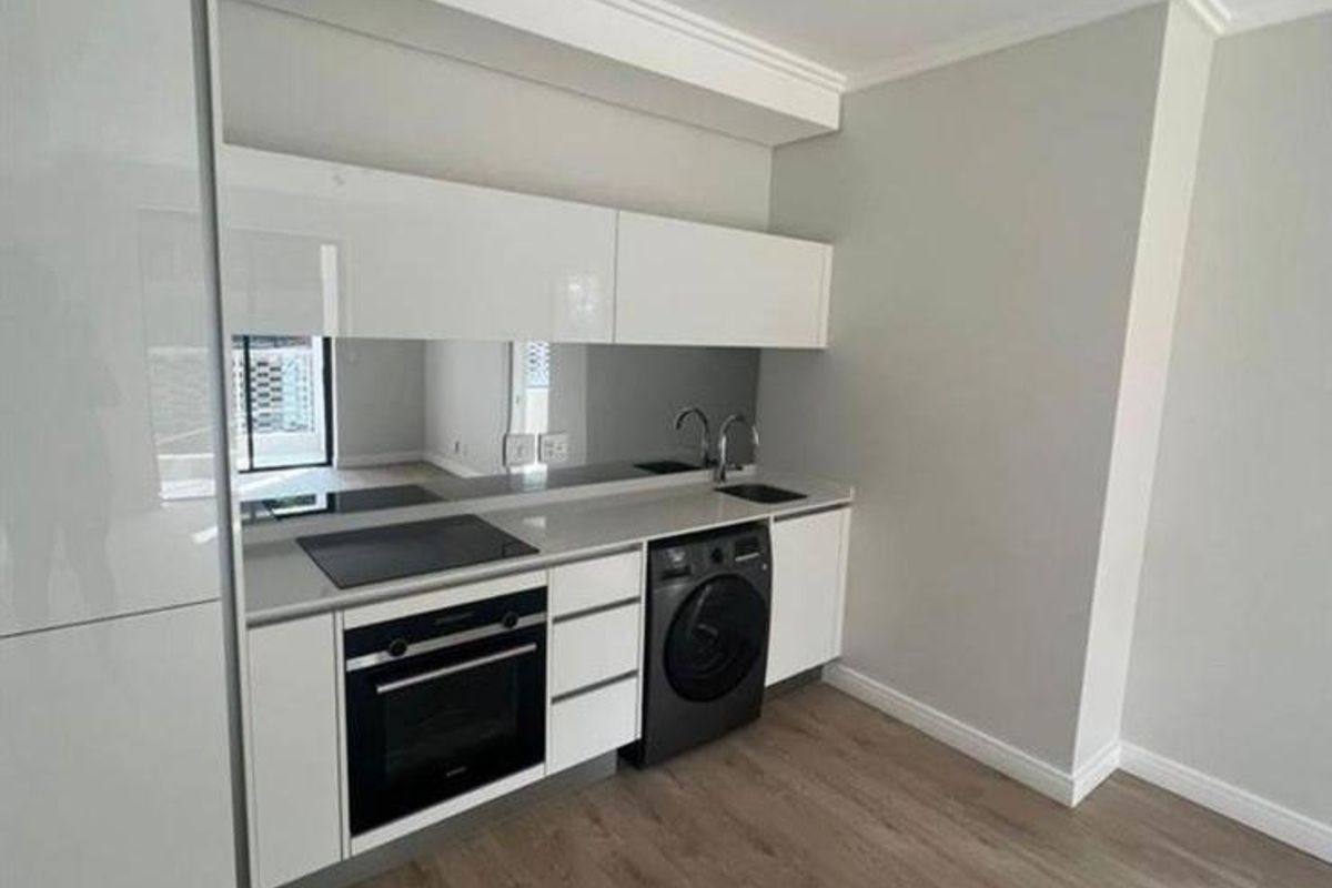 Modern kitchen featuring sleek white cabinetry, integrated oven, electric hob, and a mirrored splashback, complemented by light wood-look flooring and track lighting.