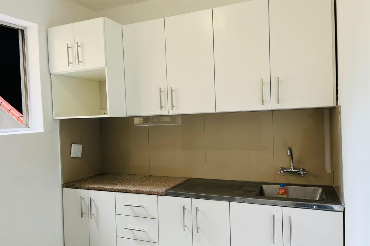 A clean, modern kitchen featuring white cabinetry, granite countertops, a stainless steel sink, and a neutral glass splashback.