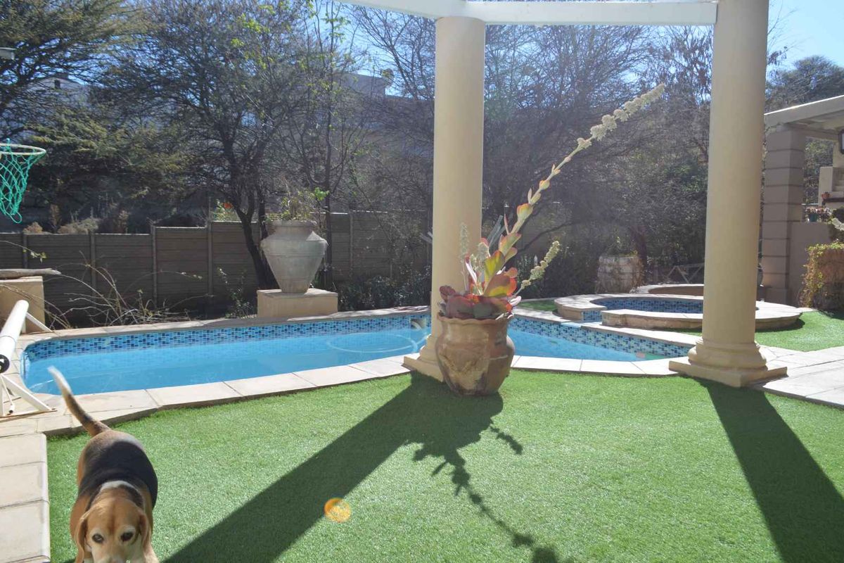 Outdoor pool area featuring a swimming pool, integrated spa, synthetic lawn, and structural columns, providing a functional space for outdoor recreation.