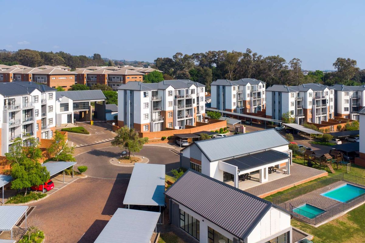 Aerial view of a modern apartment complex featuring multiple residential blocks, a swimming pool, clubhouse, and extensive covered parking facilities.