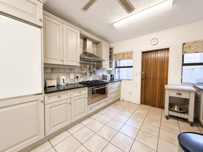 Functional kitchen featuring neutral cabinetry, granite countertops, gas hob, built-in oven, and tiled flooring with direct access to an exterior door.