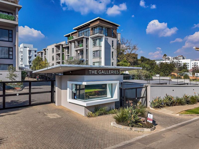The entrance to The Galleries apartment complex, featuring a modern guard house, secure gated access, and well-maintained paved driveway and perimeter fencing.