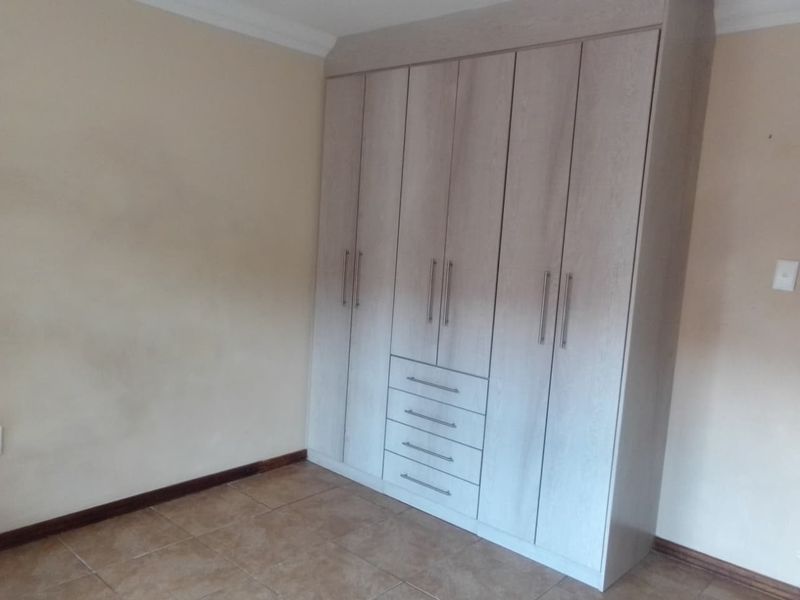 A clean, empty bedroom featuring modern light-wood built-in wardrobes with integrated drawers and neutral tiled flooring.