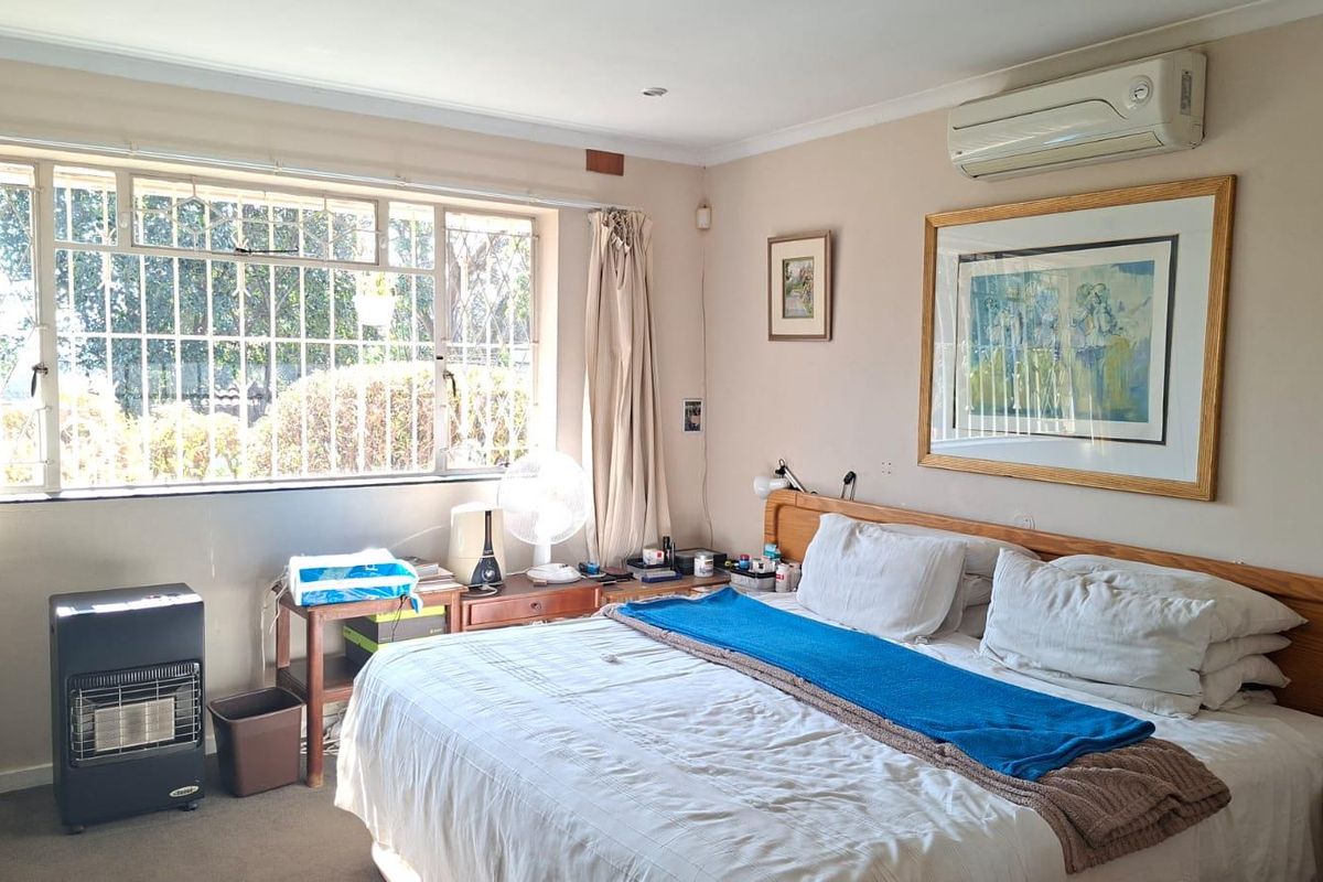A spacious bedroom featuring carpet flooring, a wall-mounted split-system air conditioner, and large windows fitted with security bars for added peace of mind.