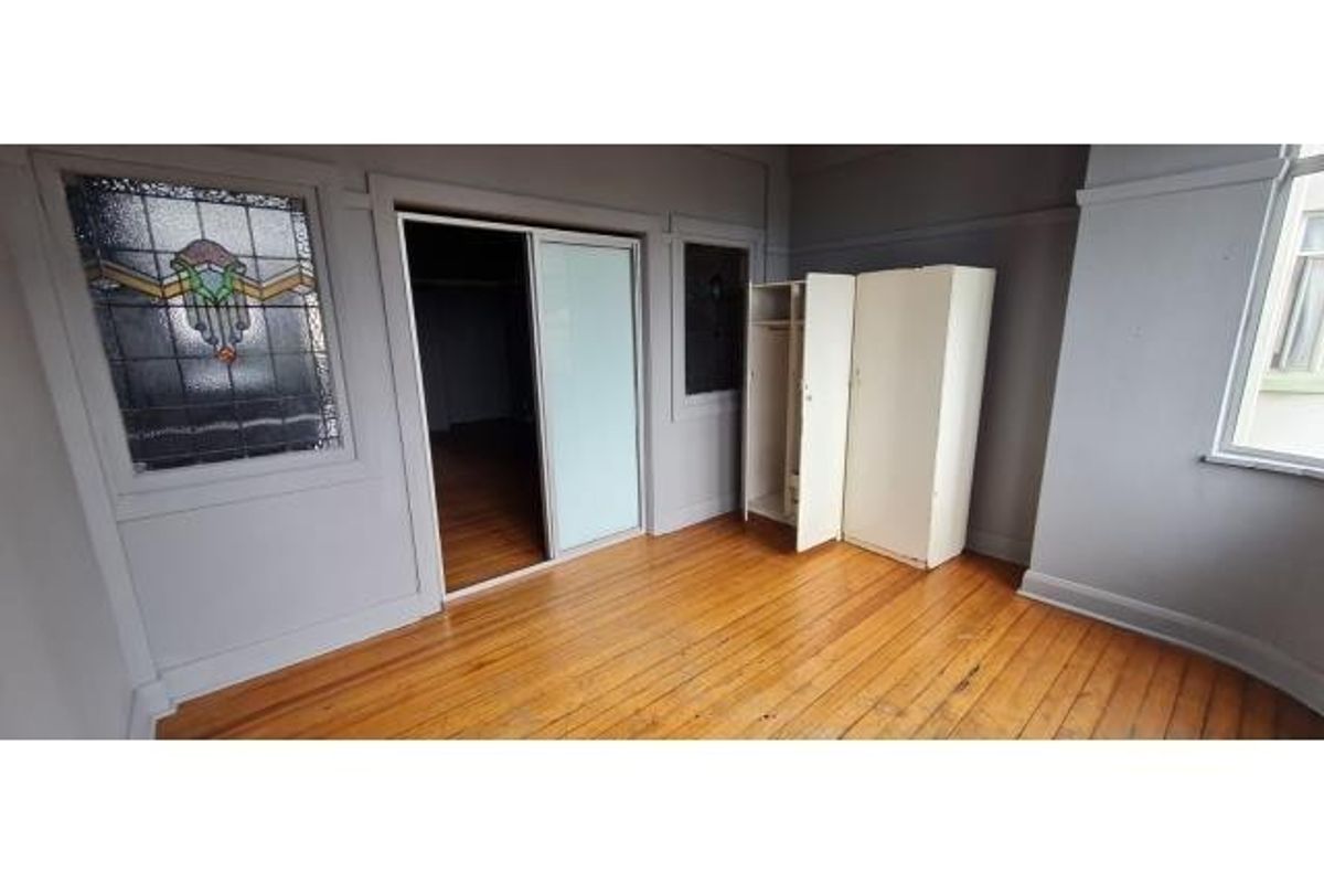 Bedroom featuring original hardwood flooring, a decorative stained glass window, and built-in closet storage.