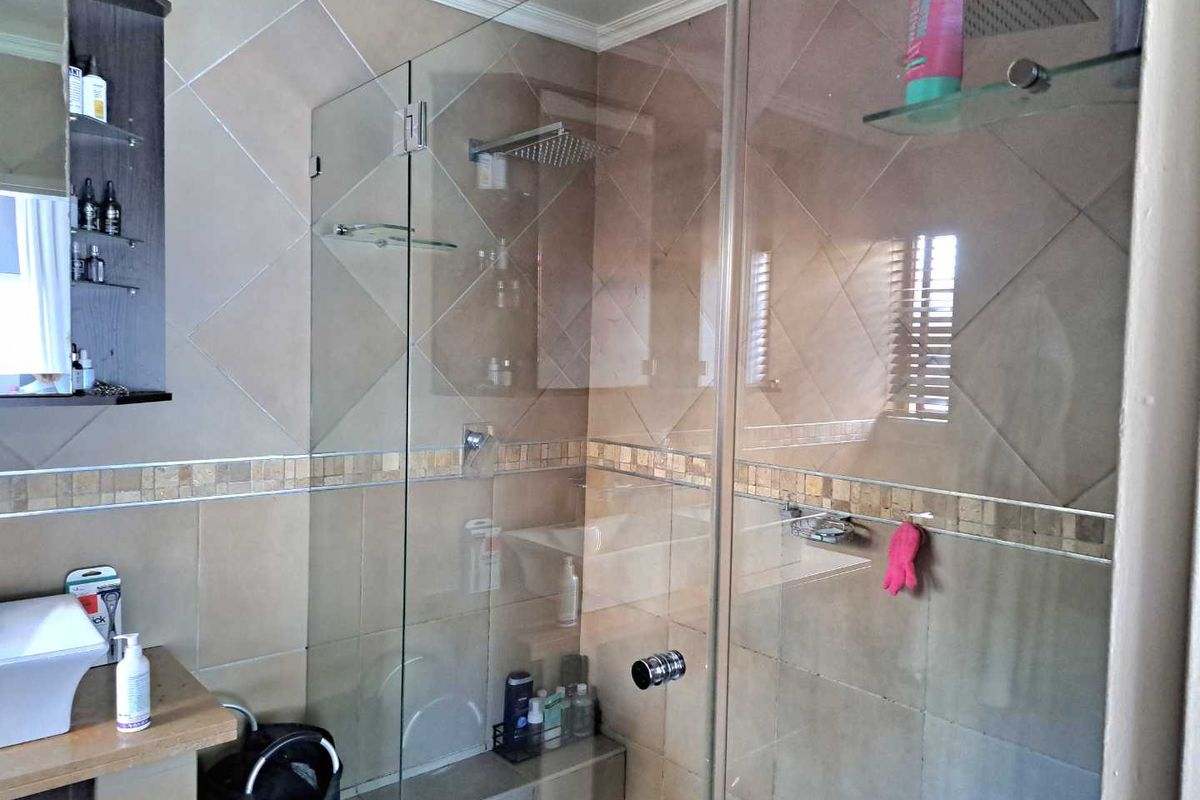 A modern bathroom featuring a glass-enclosed shower with a rain shower head, tiled walls with mosaic accents, and a contemporary vessel sink vanity.