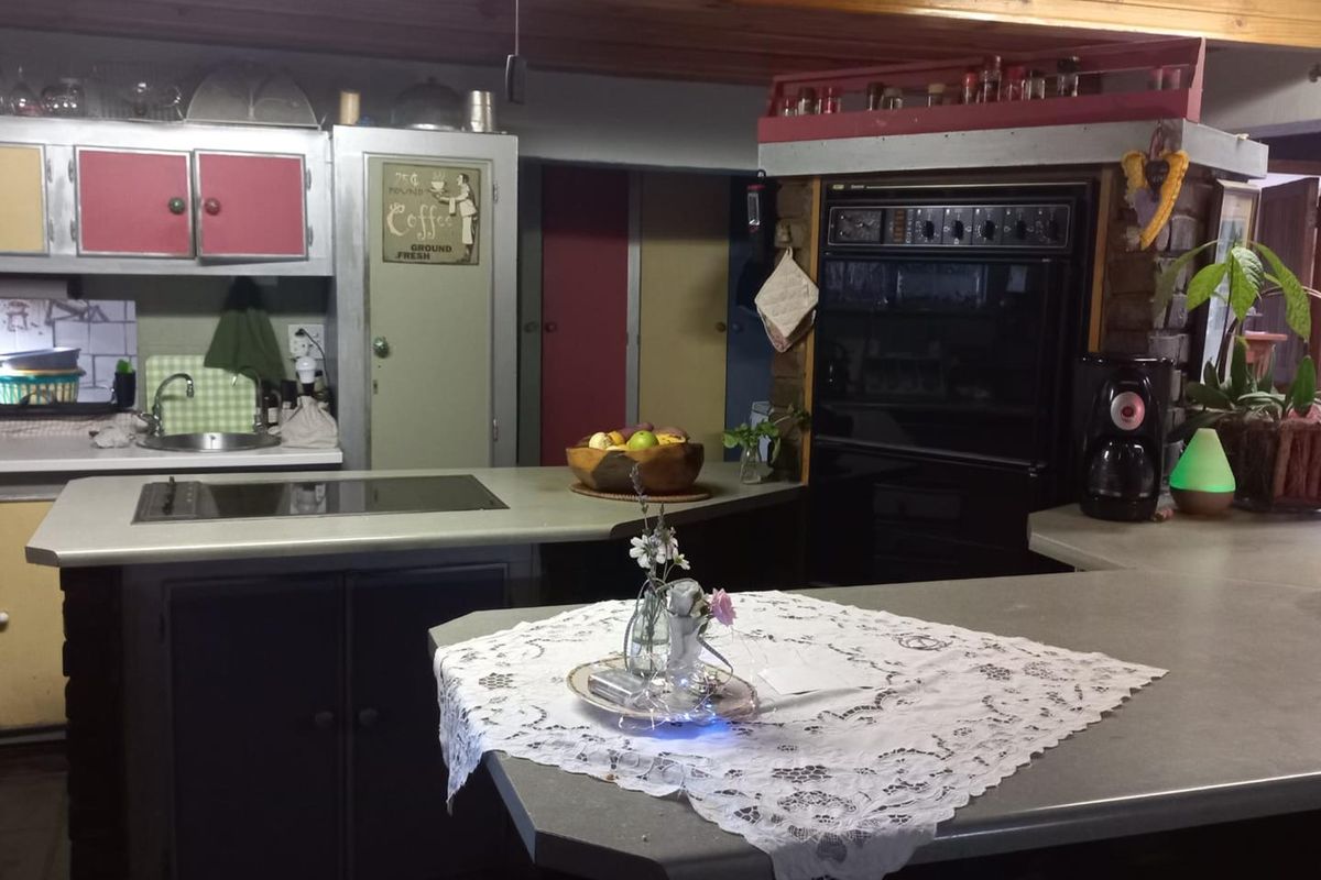 A dated kitchen featuring a central island, built-in oven, and integrated cooktop with exposed timber ceiling beams.