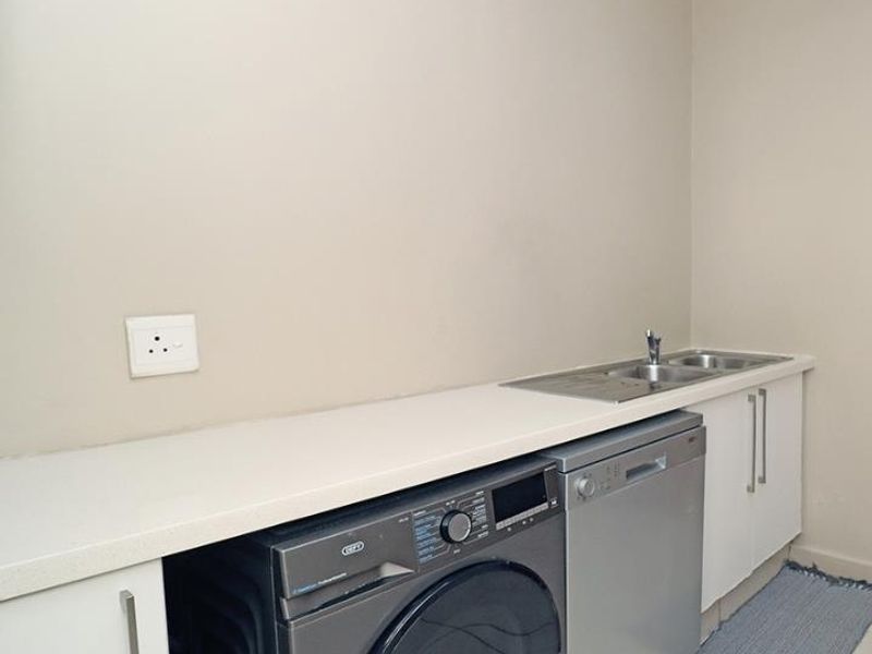 A functional laundry area featuring built-in cabinetry, a stainless steel sink, and dedicated spaces for under-counter appliances.