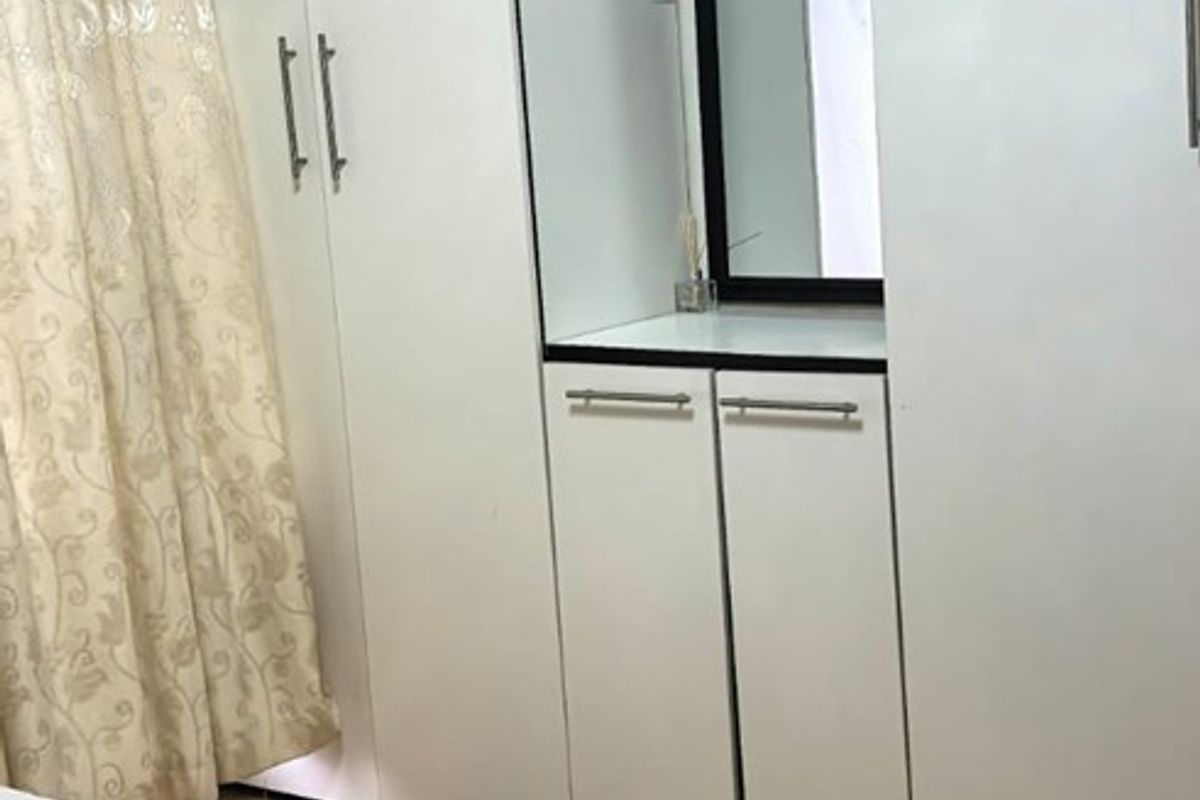 A well-maintained bedroom featuring floor-to-ceiling built-in cupboards with an integrated vanity mirror and warm-toned laminate flooring.