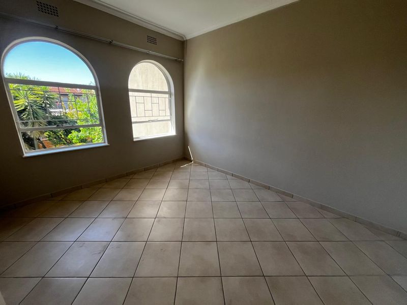 An empty bedroom featuring neutral tiled flooring, arched windows, and classic cornicing, offering a bright and versatile space ready for personalization.