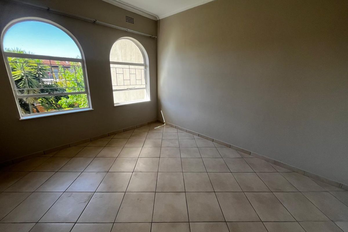 An empty bedroom featuring neutral tiled flooring, arched windows, and classic cornicing, offering a bright and versatile space ready for personalization.