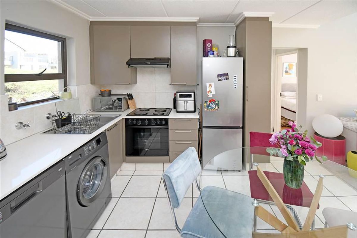 A functional kitchen featuring modern taupe cabinetry, tiled flooring, a built-in oven and hob, and an integrated laundry appliance space.