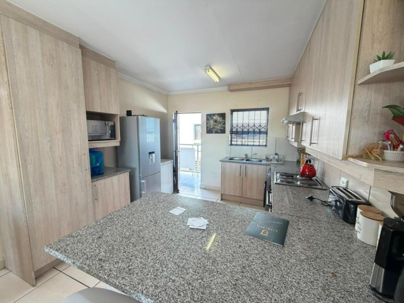 A functional kitchen featuring light wood-grain cabinetry, granite countertops, a built-in hob, and direct access to an outdoor balcony area.