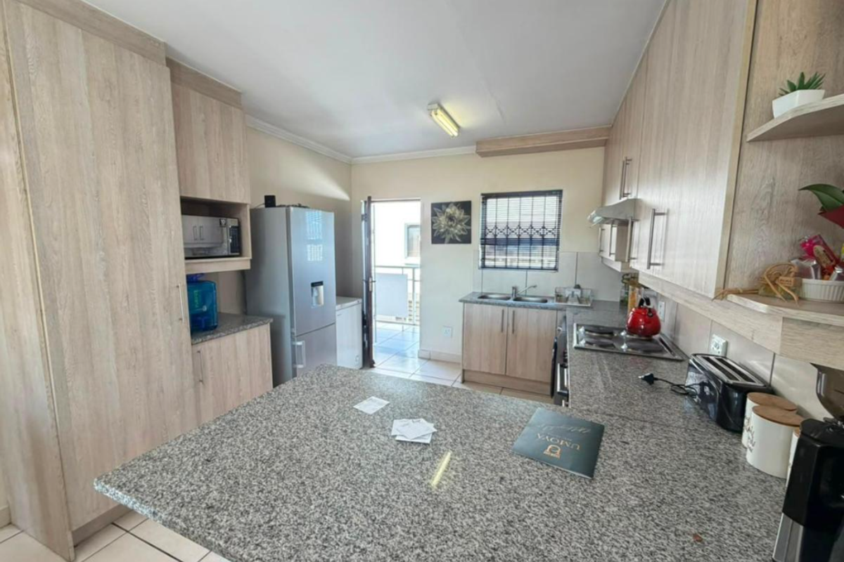 A functional kitchen featuring light wood-grain cabinetry, granite countertops, a built-in hob, and direct access to an outdoor balcony area.