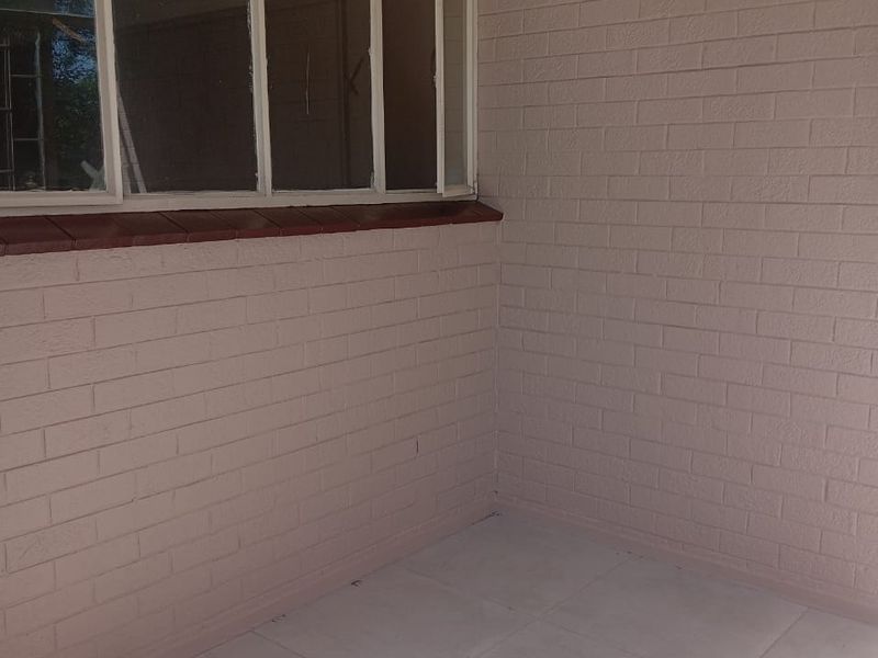 A covered balcony or patio area featuring tiled flooring and painted brick walls with steel-framed windows.