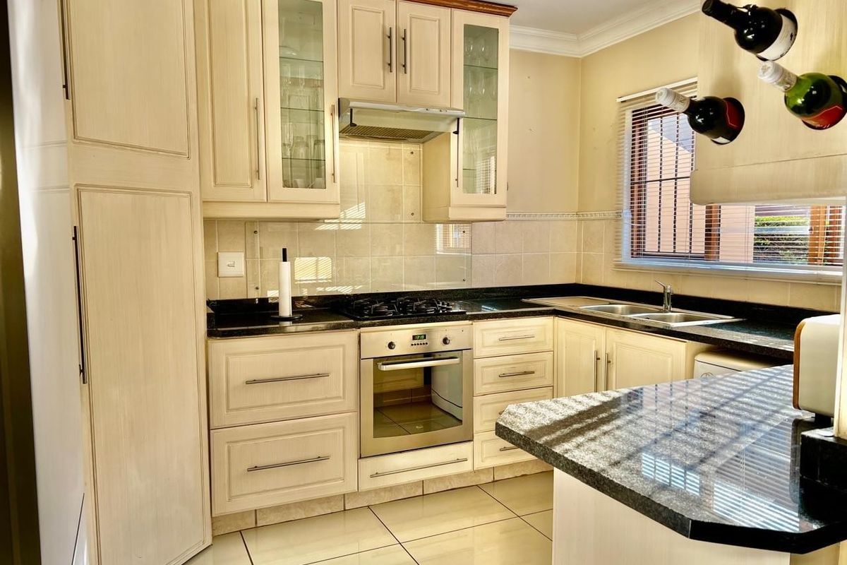 A well-maintained kitchen featuring granite countertops, built-in cabinetry, a gas hob, oven, extractor fan, and a double sink with tiled flooring.