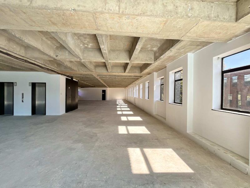 A large, open-plan office space in shell condition featuring an exposed concrete waffle ceiling, polished white walls, and multiple windows providing natural light.