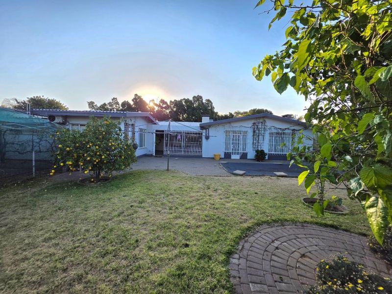 Rear view of the house featuring a paved patio area, security gates, and a well-maintained garden lawn.