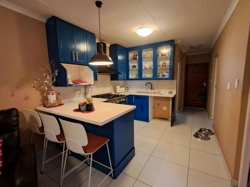 Compact kitchen featuring blue cabinetry, a gas hob, extractor fan, and a breakfast bar, finished with tiled flooring and neutral wall tones.