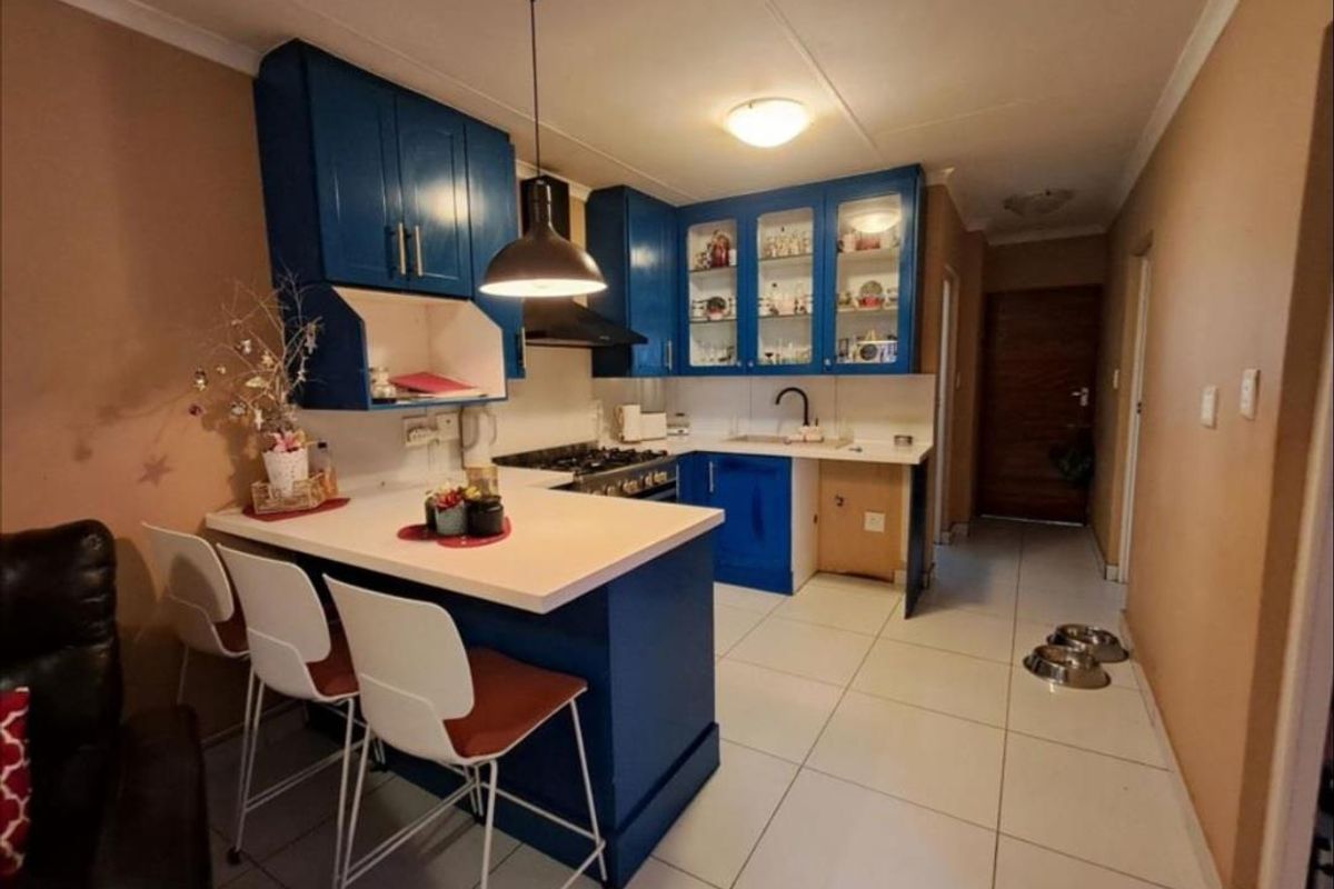 Compact kitchen featuring blue cabinetry, a gas hob, extractor fan, and a breakfast bar, finished with tiled flooring and neutral wall tones.