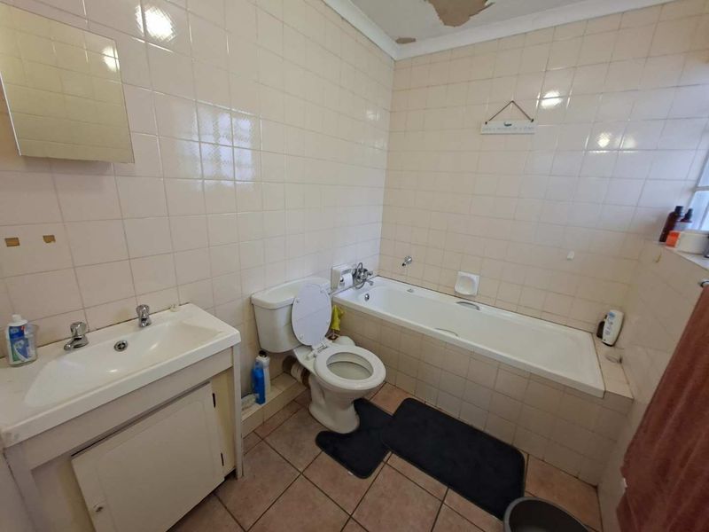 A dated bathroom featuring a built-in vanity, toilet, and bathtub with full-height wall tiling. The ceiling requires repair due to visible plaster damage.