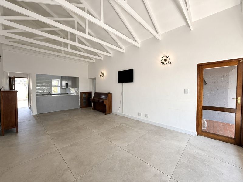 Spacious open-plan living area featuring high vaulted ceilings with exposed trusses, large format floor tiles, and a modern kitchen breakfast bar.
