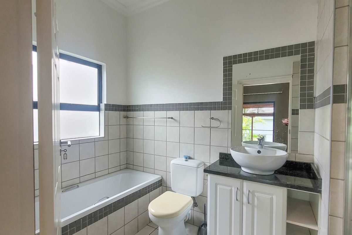 A functional bathroom featuring a built-in bathtub, a vanity with a granite countertop, a vessel sink, and tiled wall accents.