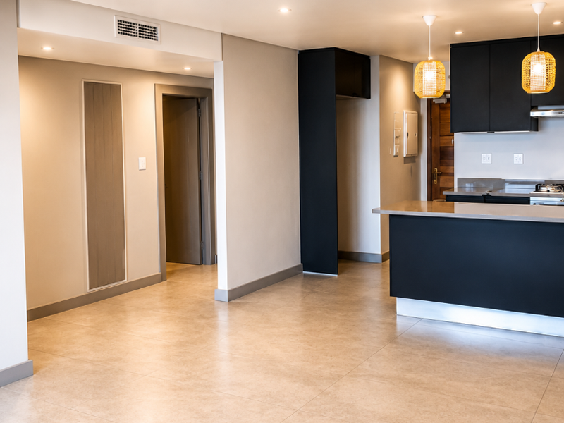 Spacious open-plan living area featuring modern dark kitchen cabinetry, stone countertops, integrated appliances, recessed lighting, and neutral tiled flooring throughout.