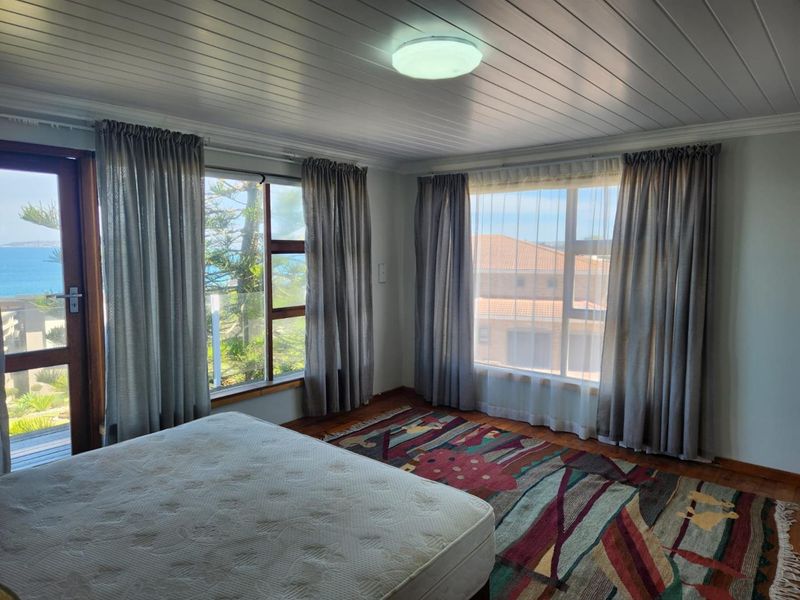 A bright bedroom featuring timber ceilings, large windows with natural light, and direct access to an outdoor area with coastal views.