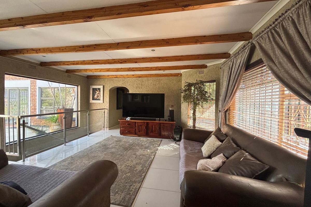 Spacious living room featuring exposed timber ceiling beams, large windows with natural light, and modern tiled flooring.