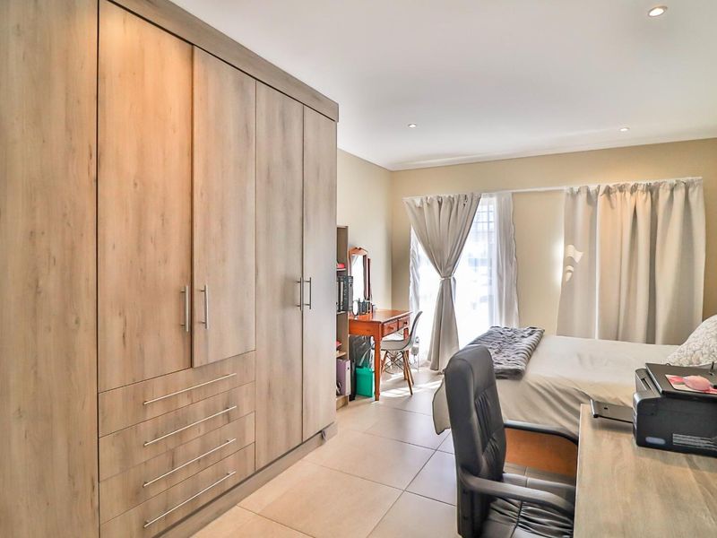 A well-maintained bedroom featuring modern wood-finish built-in wardrobes, neutral tiled flooring, and recessed downlighting.