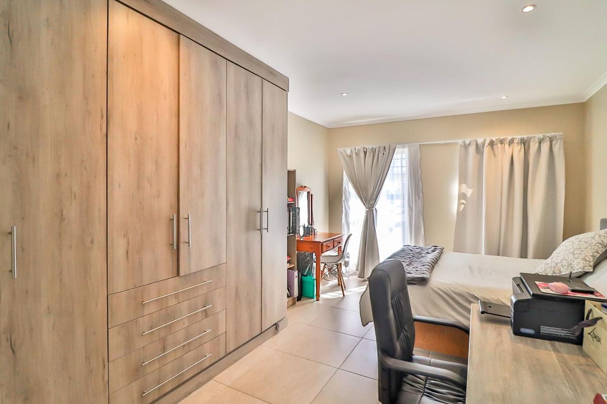 A well-maintained bedroom featuring modern wood-finish built-in wardrobes, neutral tiled flooring, and recessed downlighting.