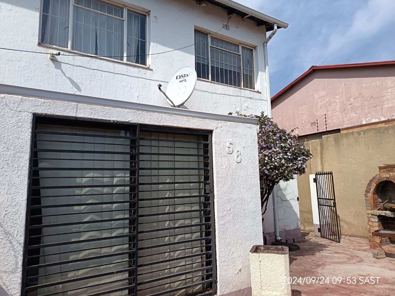 Front exterior view of a townhouse featuring security gates, metal window frames, and a built-in brick braai area in the side courtyard.